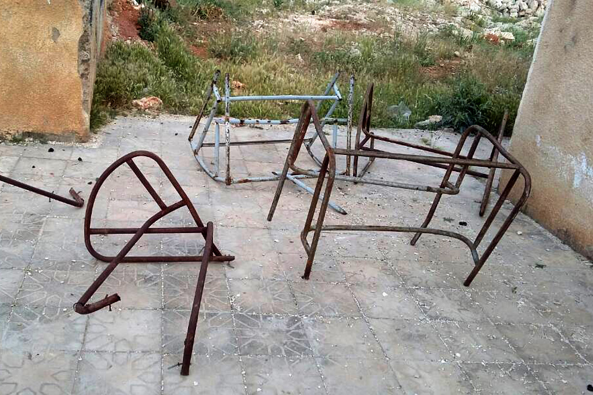 Verrostete Gestelle von Schultischen und Stühlen liegen auf dem Hof einer ehemaligen Schule.