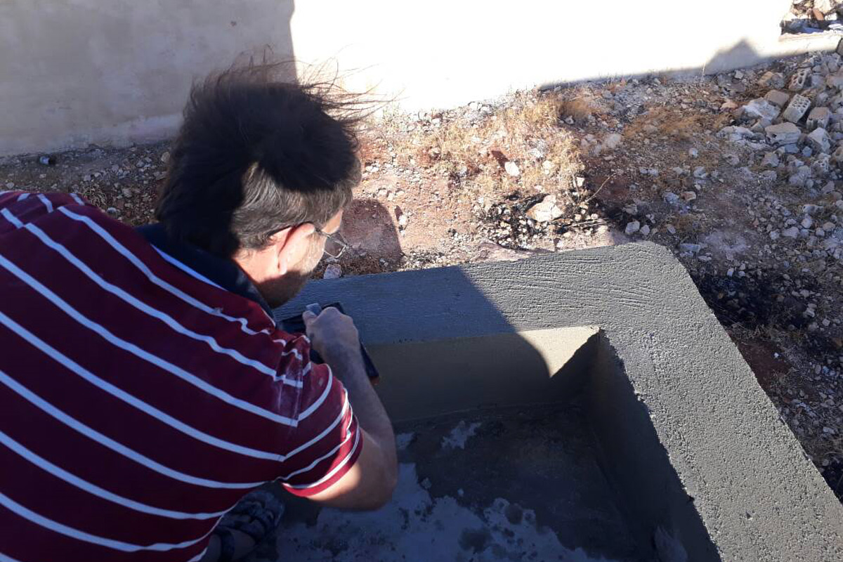 Ein Mann verputzt eine niedrige Mauer draußen vor der Schule.