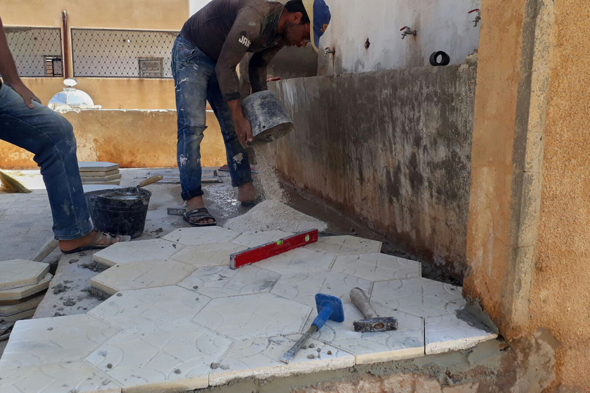 Zwei Männer verlegen neue Fliesen im Hof der Schule.