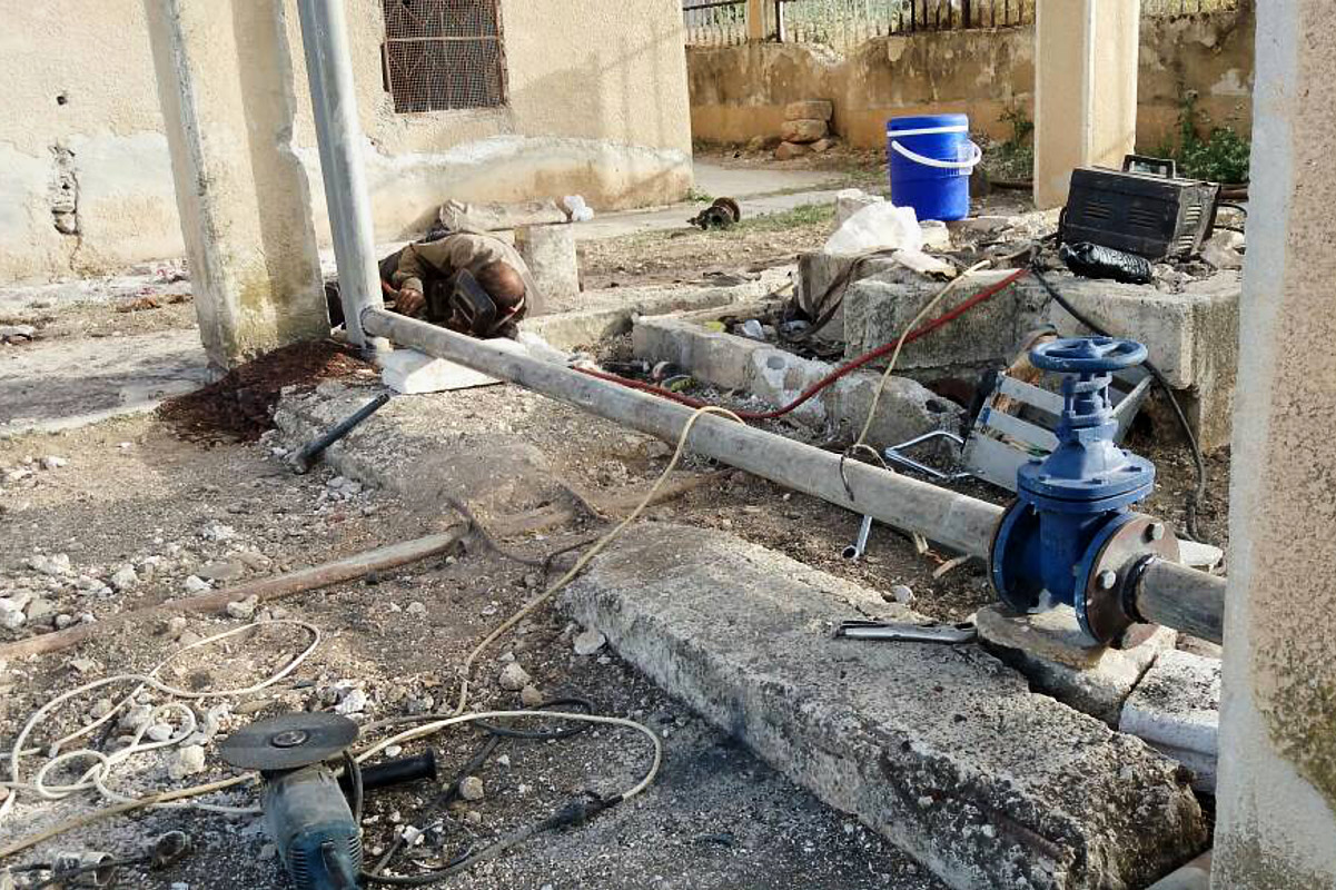 Ein Mann montiert eine Rohrleitung. Vorn hat die Leitung in großes blaues Ventil.