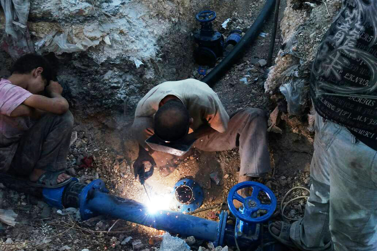 Zwei Männer arbeiten an einem Brunnen. Einer schweißt an einer blauen Rohrleitung.